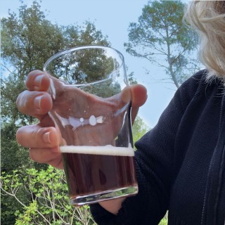 A hand holds up a glass of brown beer